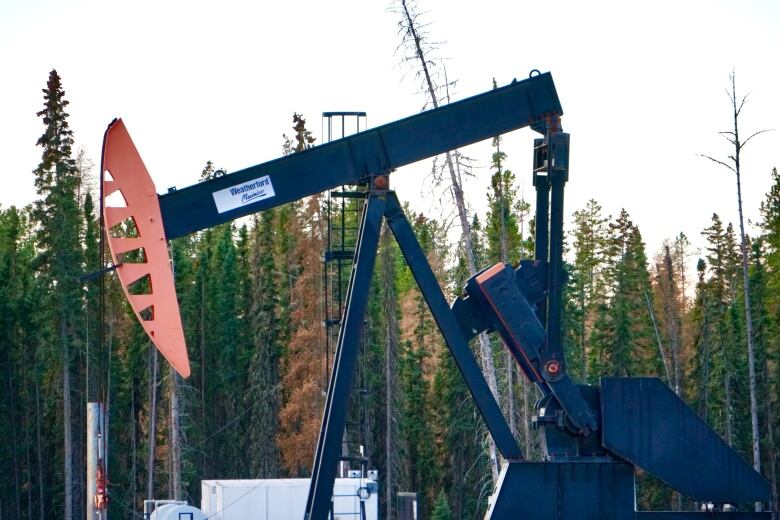 A pumpjack is pictured surrounded by trees.