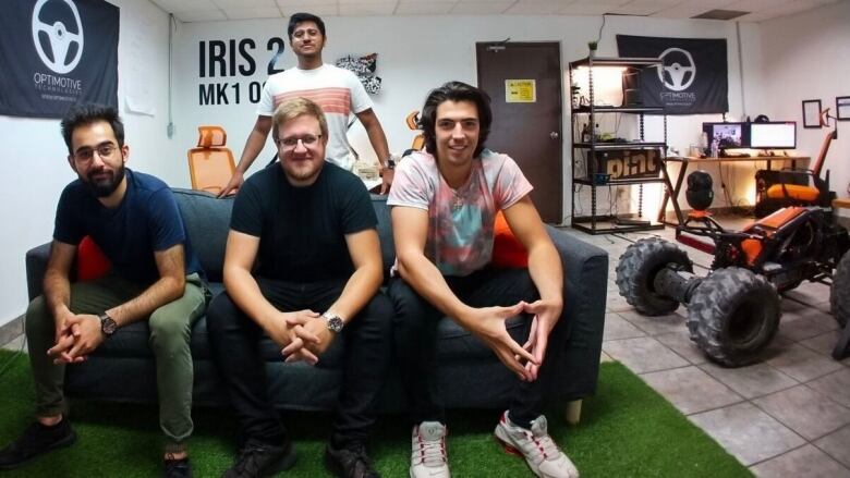 Three men sitting on a couch and one man standing behind the couch