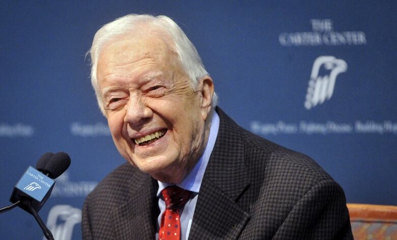 An elderly man smiles broadly during a news conference.