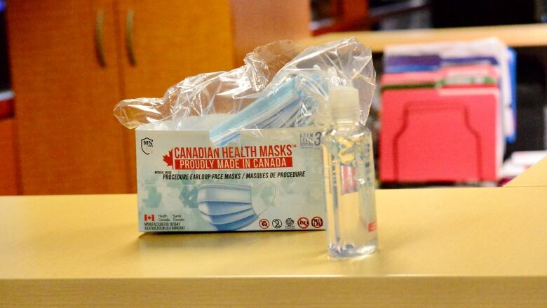 A box of masks and sanitizer sits on a table. 