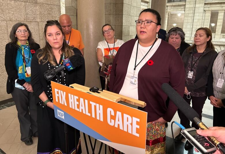 A woman speaks at a podium that says, 'fix health care' as a group of people surround her.