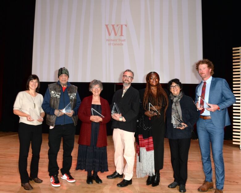 Seven people on stage smiling after an awards ceremony.