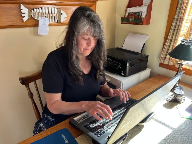 A woman is seen typing on a laptop at her desk in her home.