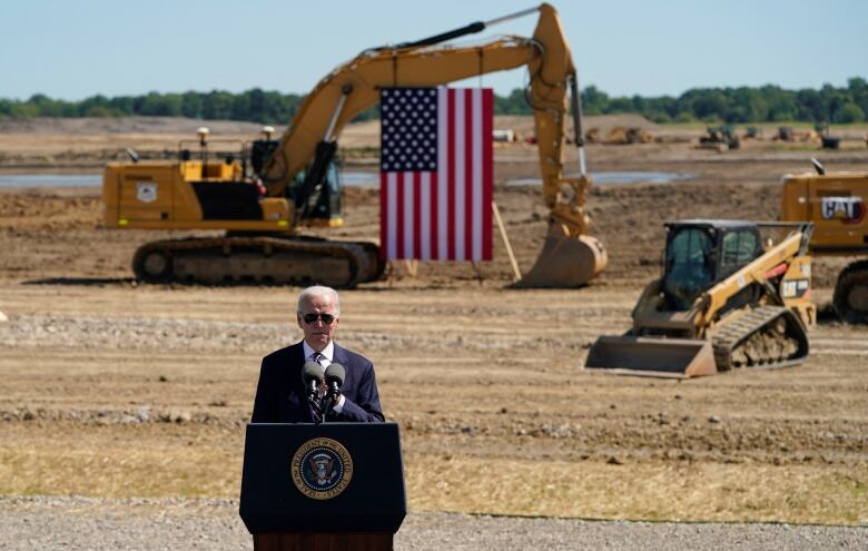 Joe Biden speaks in front of an American flag and construction site.