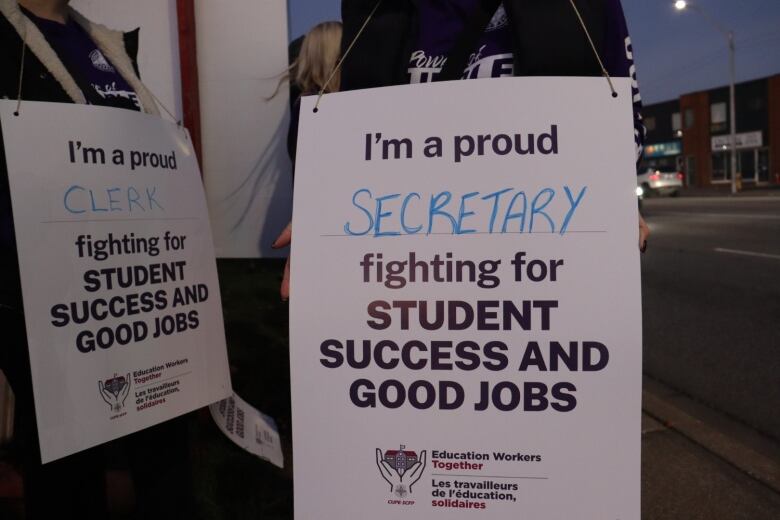 Two people hold signs, their faces hidden. The sign says 'I'm a proud secretary fighting for student success and good jobs.'