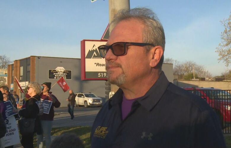 A man wearing sunglasses stands in front of protesters. 