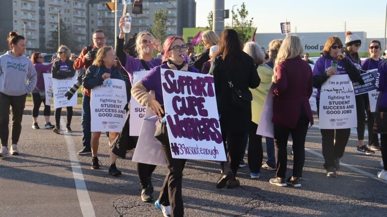 A group of picketers cross the street holding various signs.