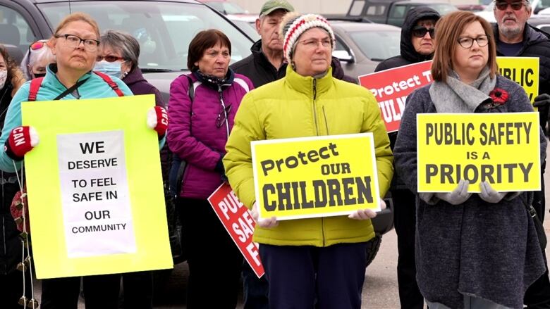 Three women hold signs while others stand behind them. 