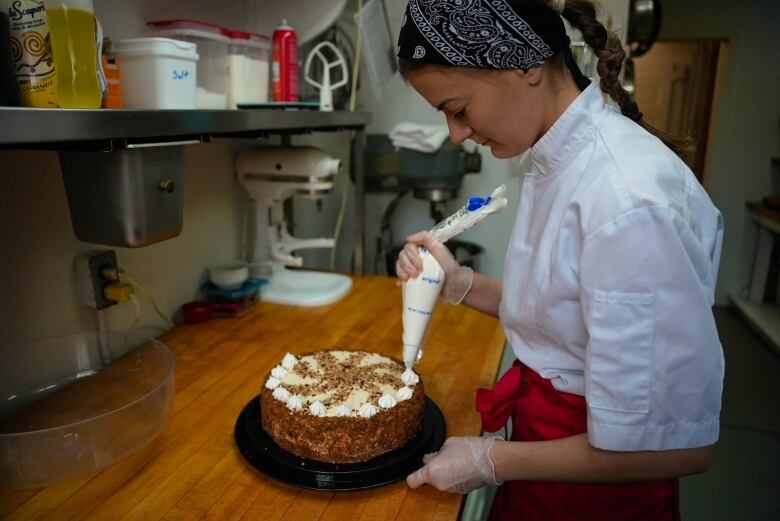 A woman decorates a cake in a large kitchen.