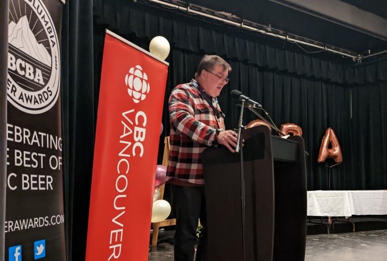 Stephen Quinn, a white man wearing spectacles, stands at a podium.