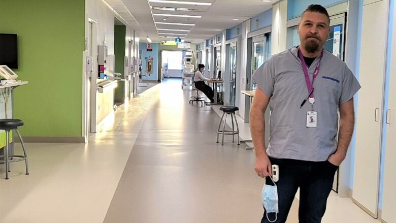 A man holding a surgical mask stands in the middle of a hospital hallway. 