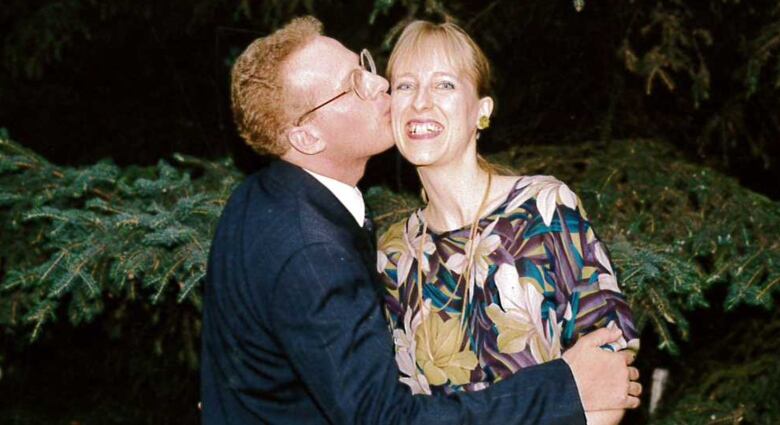 A woman smiles at the camera while a man kisses her on the cheek. 