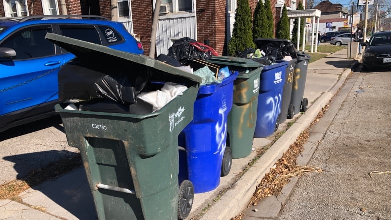 Garbage pails filled with garbage sit at the curb on University Ave. W. waiting for pickup.