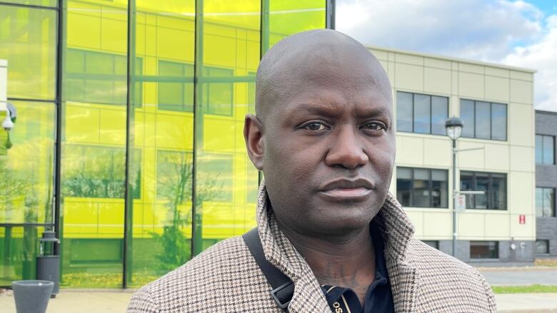 Portrait of man with a serious expression outside a building of greenish glass.