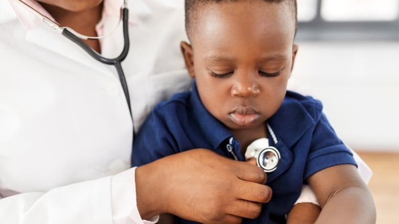 A closeup of a toddler being examined by a doctor holding a stethoscope to the young boy's chest.