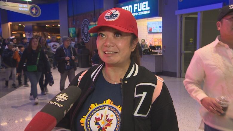 A Filipina woman in a Winnipeg Jets jersey with a new Filipino-inspired logo smiles as she talks to a reporter inside the team's arena.