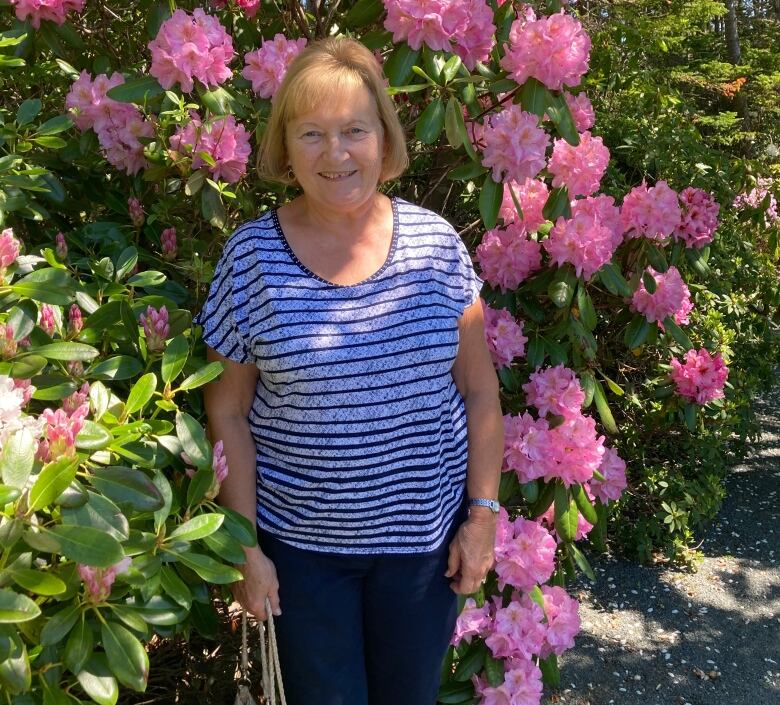 A woman poses in front of a blooming pink-flowered bush. 