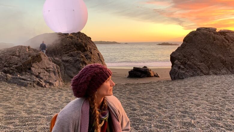 Woman looks off into the sunset as she sits on a beach. 