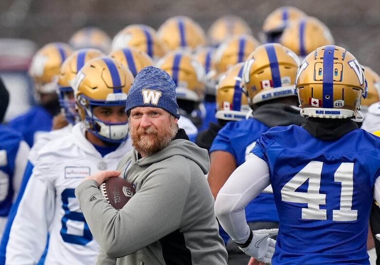 Surrounded by his players, Winnipeg Blue Bombers head coach Mike O'Shea walks with the football during practice ahead of the 108th CFL Grey Cup against the Hamilton Tiger-Cats in Hamilton, Ont., on Wednesday, Dec. 8, 2021.