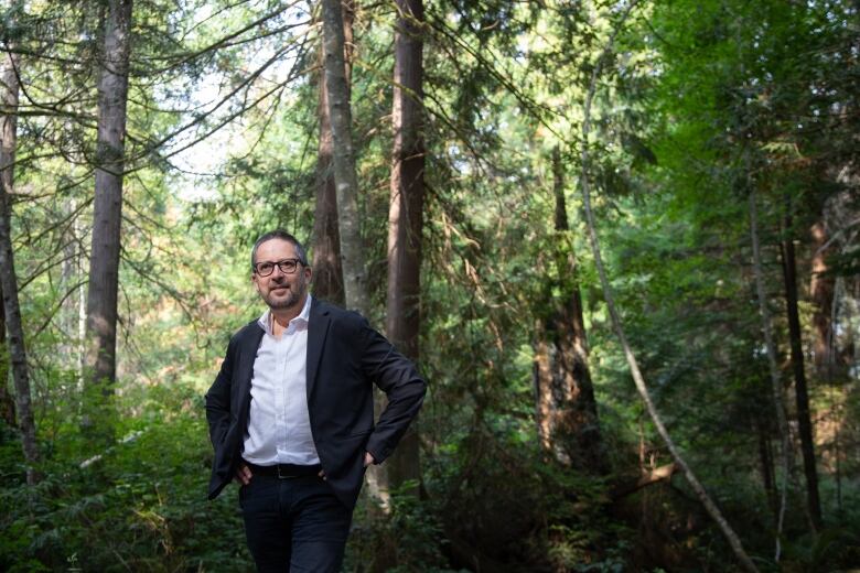 Man in suit stands in front of a lush, green forest backdrop