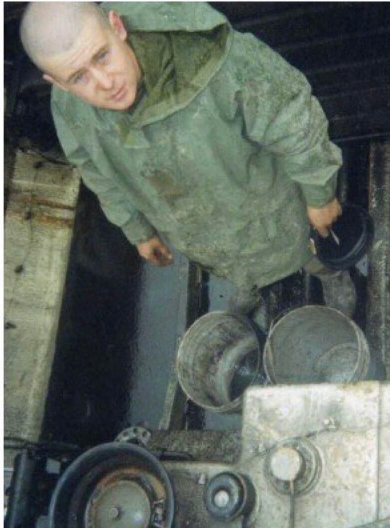 A person in uniform, inside a military tank, looking up at the camera.