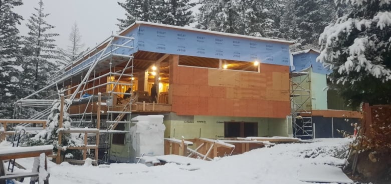 A partially constructed home without windows surrounded by a layer of fresh snow. 