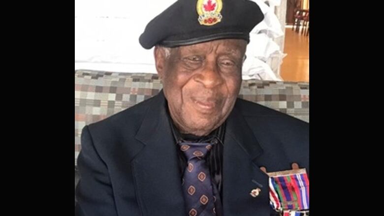 An older Black man wearing a military hat and badges on his suit