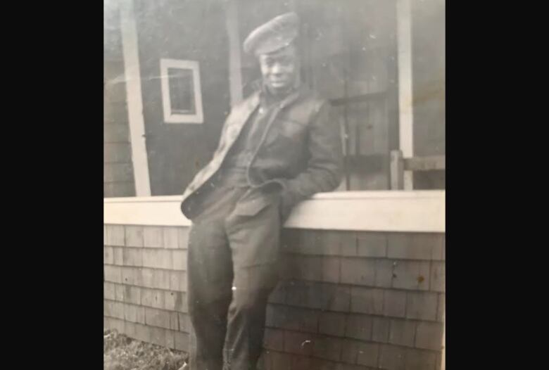 An old photo of a Black man wearing army garb and leaning against a wall