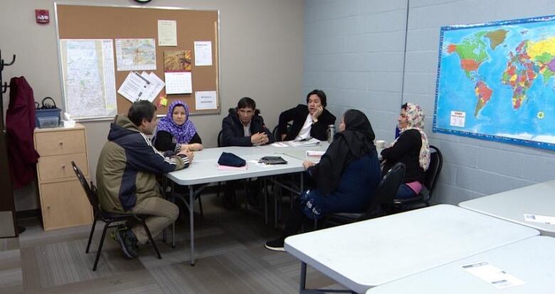 A group of people sit around a table with a world map on the right wall.