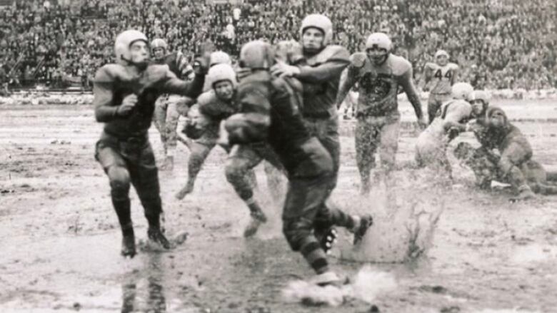 Black and white photo of football players covered in mud, playing in a wet and dirty field.