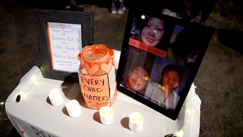 A table has photographs and names on it with a jar that says every child matters. There are also four electric candles and a string of lights. 