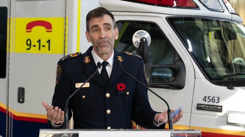 A man in a uniform stands in front of an ambulance with his palms out and facing up. 