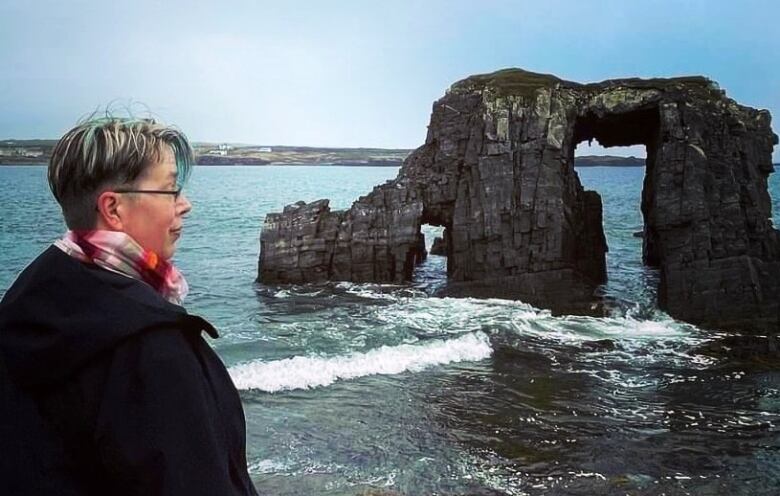 A person is standing in front of the ocean, facing away from the camera.