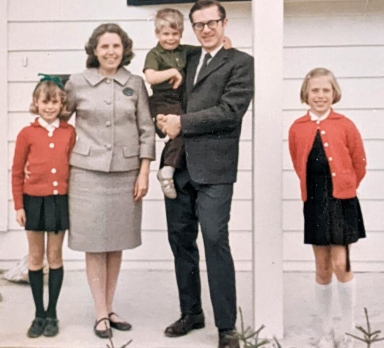 A family of five is pictured in front of a partly-pictured white house  a mother and father with three young children. The photo is old and very pixelated.