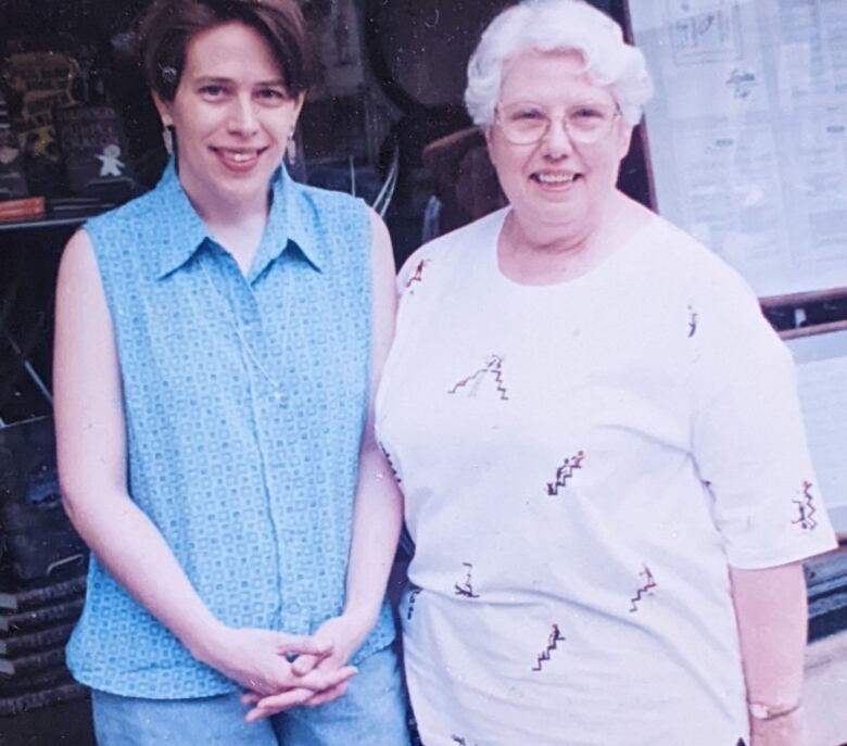 A middle-aged adult and an older woman stand next to each other, smiling into the camera.