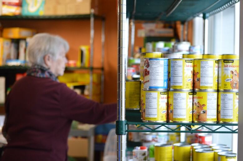 A line of cans on a shelf with a woman reaching for one in the background