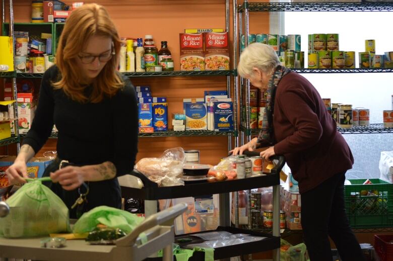 A woman holds a plastic bag in a room surrounded by packaged food