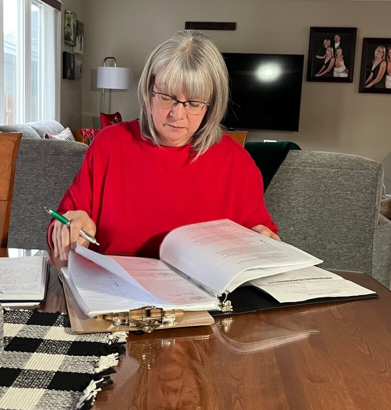 A middle-aged woman sits at a table, looking through documents in front of her.