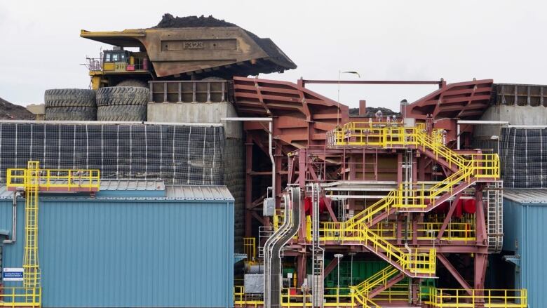 Buildings and stairs are shown in the foreground while a large dump truck waits to dump its load on top.