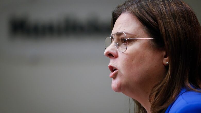 A close-up profile view of a woman wearing glasses and a bright blue blazer.