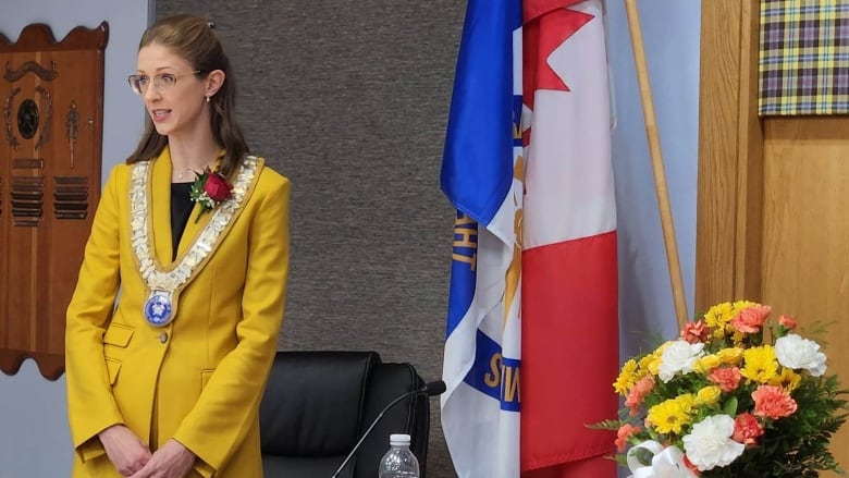 Timmins Mayor Michelle Boileau addresses the council chambers wearing the chain of office and a yellow suit, while a judge looks on. 