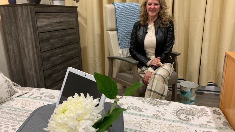 A blonde woman sits in a modern, comfortable hospital room. 