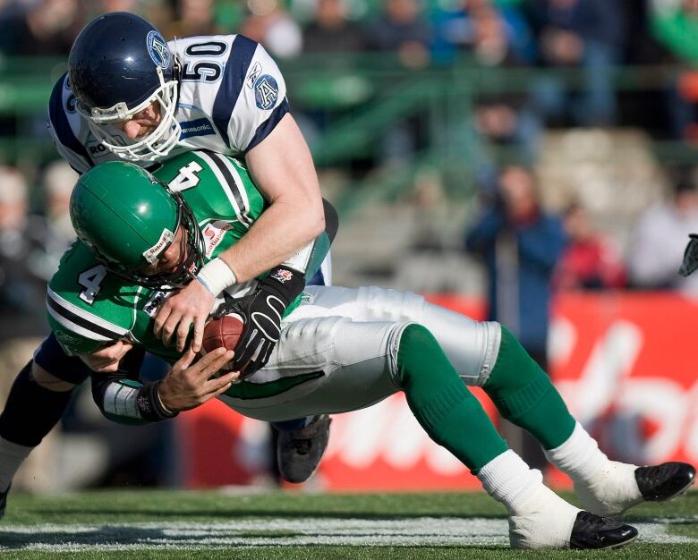 A football player in a blue and white uniform tackles one in a green and white uniform.