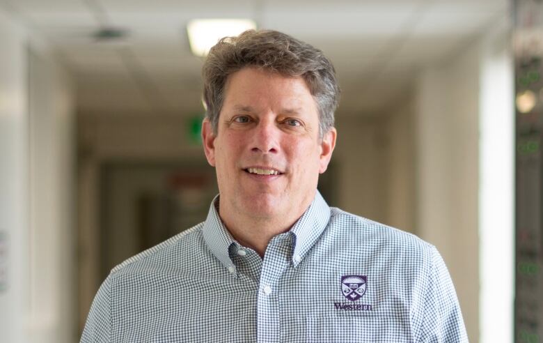 A man with brownish grey hair wears a blue and white checked shirt.