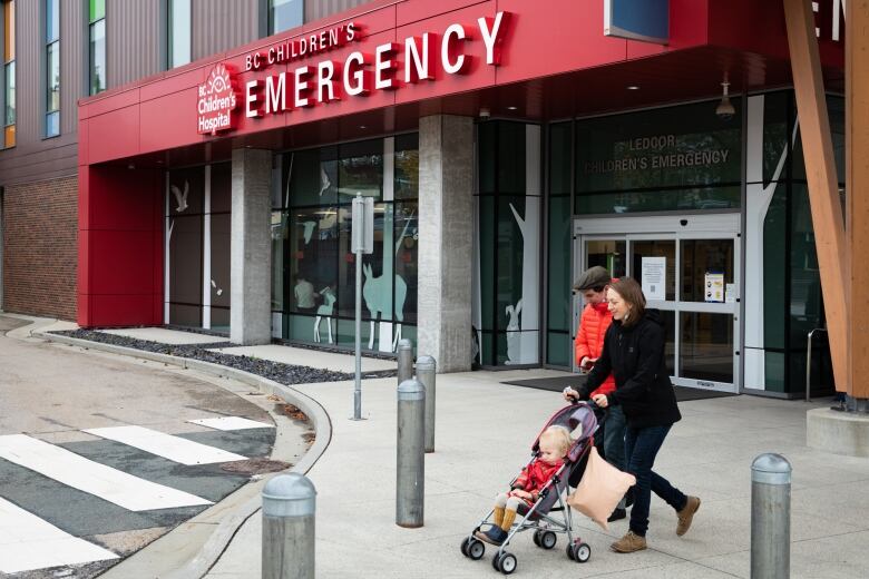 A couple with a stroller walk in front of BC Childrens Hospital Emergency Department.