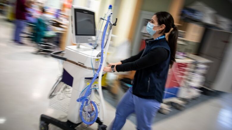 a doctor wearing a mask walks through a hospital wearing a mask and pushing a cart. 