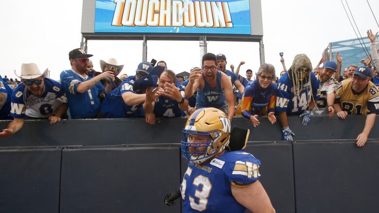 Fans in the stands cheer in front of a large screen reading 