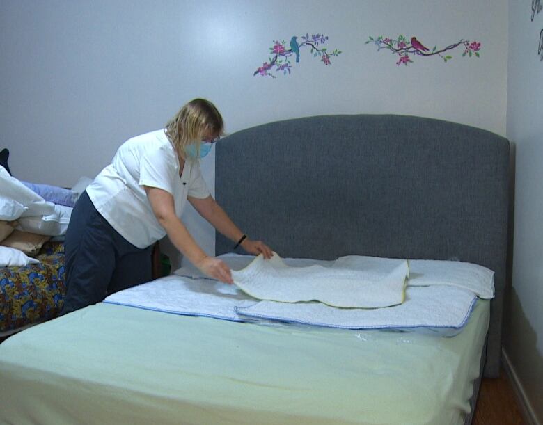 A middle-aged woman is placing several bedwetting mats on a mattress.