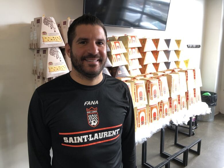 A man smiles in front of a wall of panettones. 