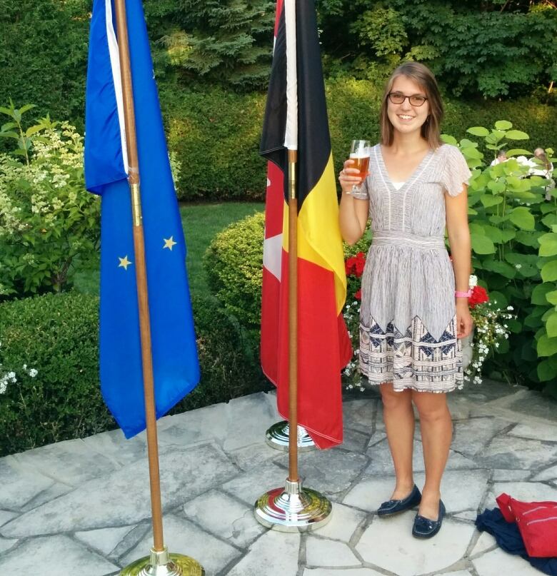 A woman holds a Beer in front of the Belgian flag. 